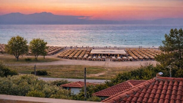 A beachside view with a restaurant, umbrellas, and a mountainous backdrop. - Heraklia villa sea view pool & jacuzzi (XALKIDIKI)