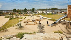 Een speeltuin met zand, boomstammen en een glijbaan.