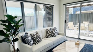 Een moderne woonkamer met een bank, gekleurde kussens, een salontafel en een grote potplant.