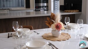 Een moderne keuken met een wit aanrecht, roestvrijstalen apparatuur en een eethoek met wit servies en glazen.