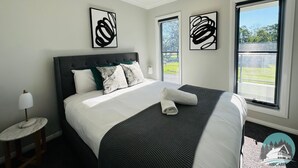 Een moderne hotelkamer met een groot bed, twee ramen en abstracte kunst aan de muren.