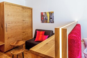 Una habitación moderna con un armario de madera, una mesita redonda pequeña, un sofá con un cojín rojo y un cuadro en la pared.