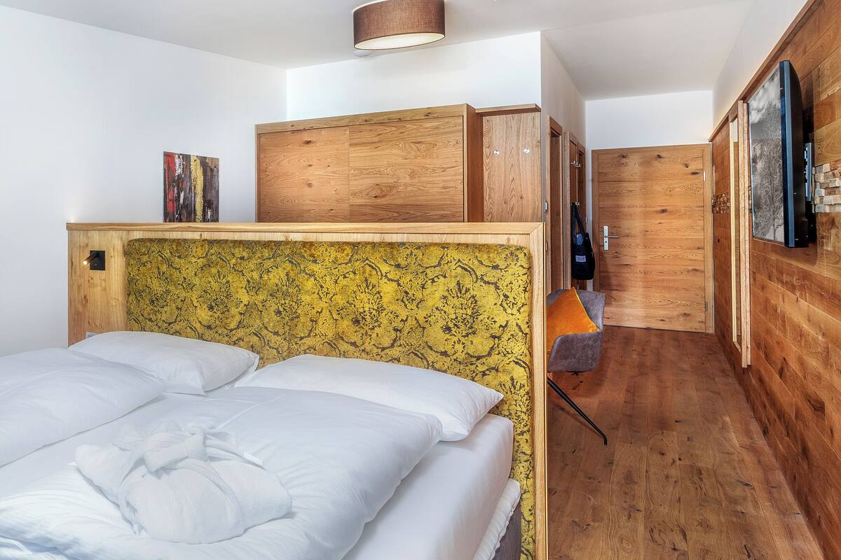 Une chambre à coucher avec une tête de lit en bois, un lit recouvert de draps blancs, une armoire en bois et un téléviseur fixé au mur.