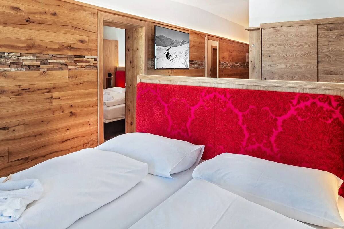 Une chambre à coucher avec une tête de lit en bois, un lit recouvert de draps blancs et un plaid rouge à motifs.