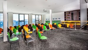 Une salle de conférence avec plusieurs rangées de chaises, de grandes fenêtres donnant sur les montagnes et un projecteur au plafond.
