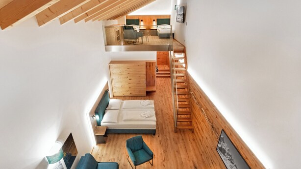 Une chambre moderne de style loft, dotée d’un plancher en bois, d’un canapé, d’un fauteuil, d’un lit et d’un escalier menant à un niveau supérieur.