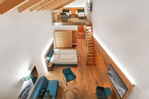 Un moderno espacio tipo loft con piso de madera, un sofá, una silla, una cama y una escalera que conduce a un nivel superior.