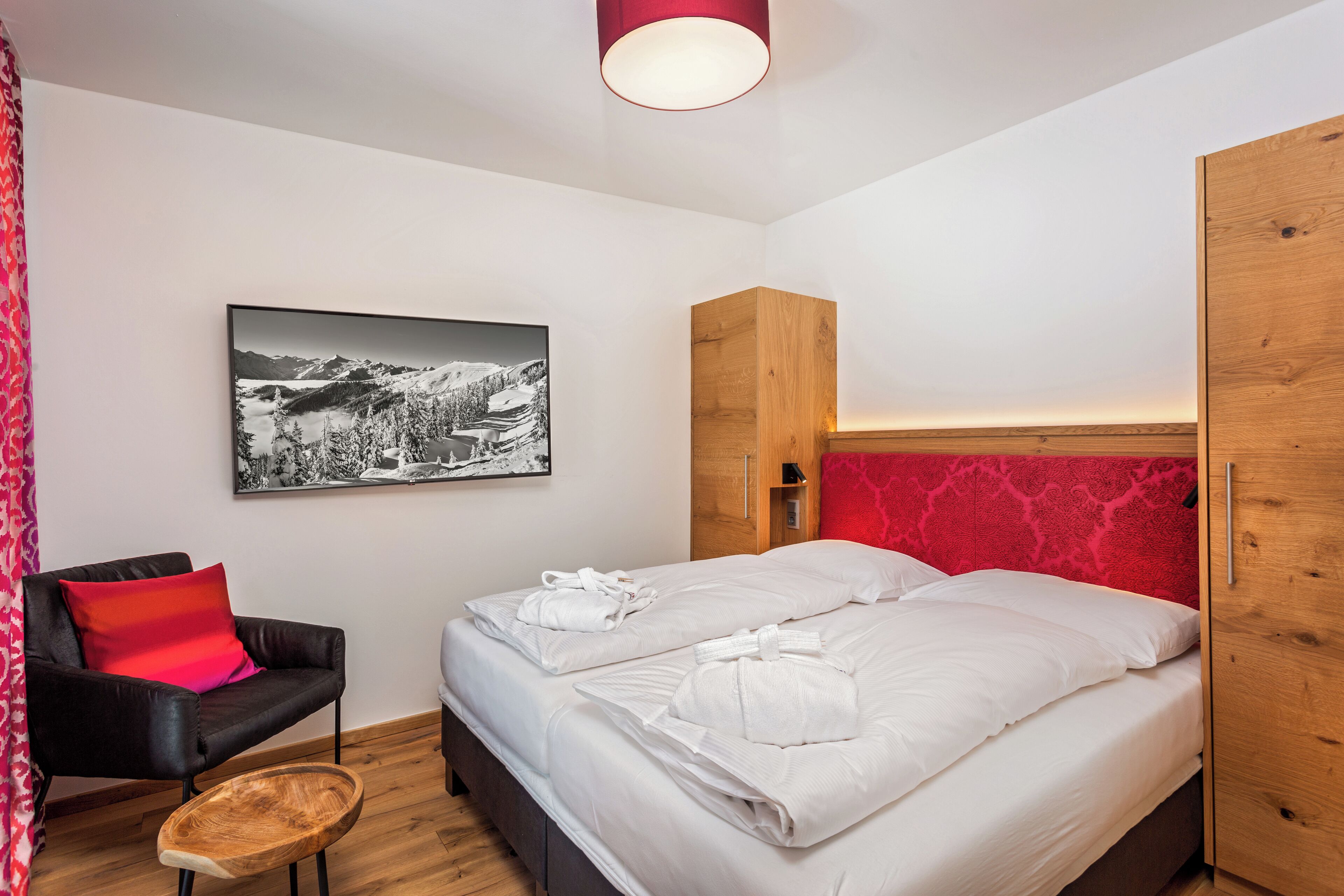 Ett modernt hotellrum med en säng, en stol, en garderob i trä och en inramad tavla på väggen.