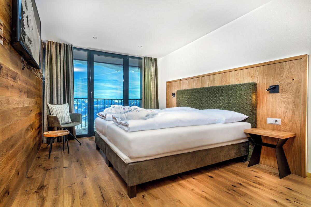 Une chambre d’hôtel moderne avec un grand lit, un plancher en bois, une vue sur le ciel et un balcon.