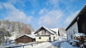 Una casa a due piani con un tetto spiovente, una stalla di legno e un paesaggio innevato.
