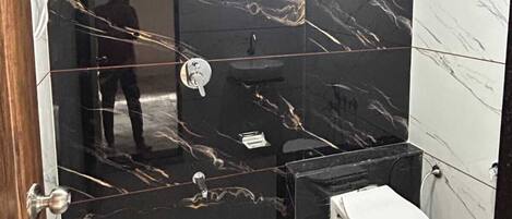 A modern bathroom with black marble walls, a white toilet, and a sink.