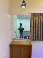 A mirror reflecting a person taking a selfie, a wooden cabinet, and a patterned curtain.