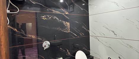 A modern bathroom with black marble walls, a white toilet, a green trash bin, and a white sink.