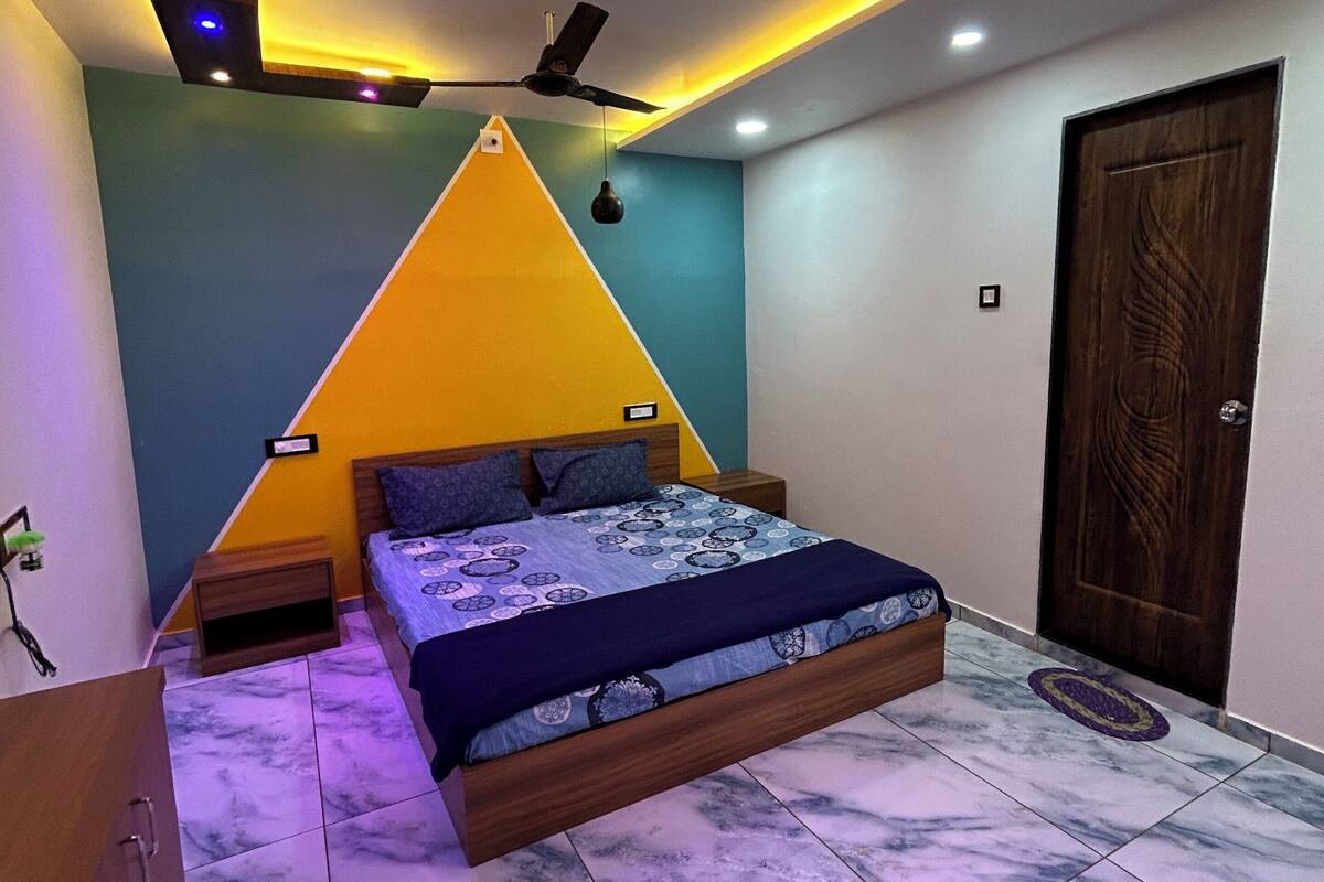 A bedroom with a bed, a ceiling fan, a wooden door, and a nightstand.