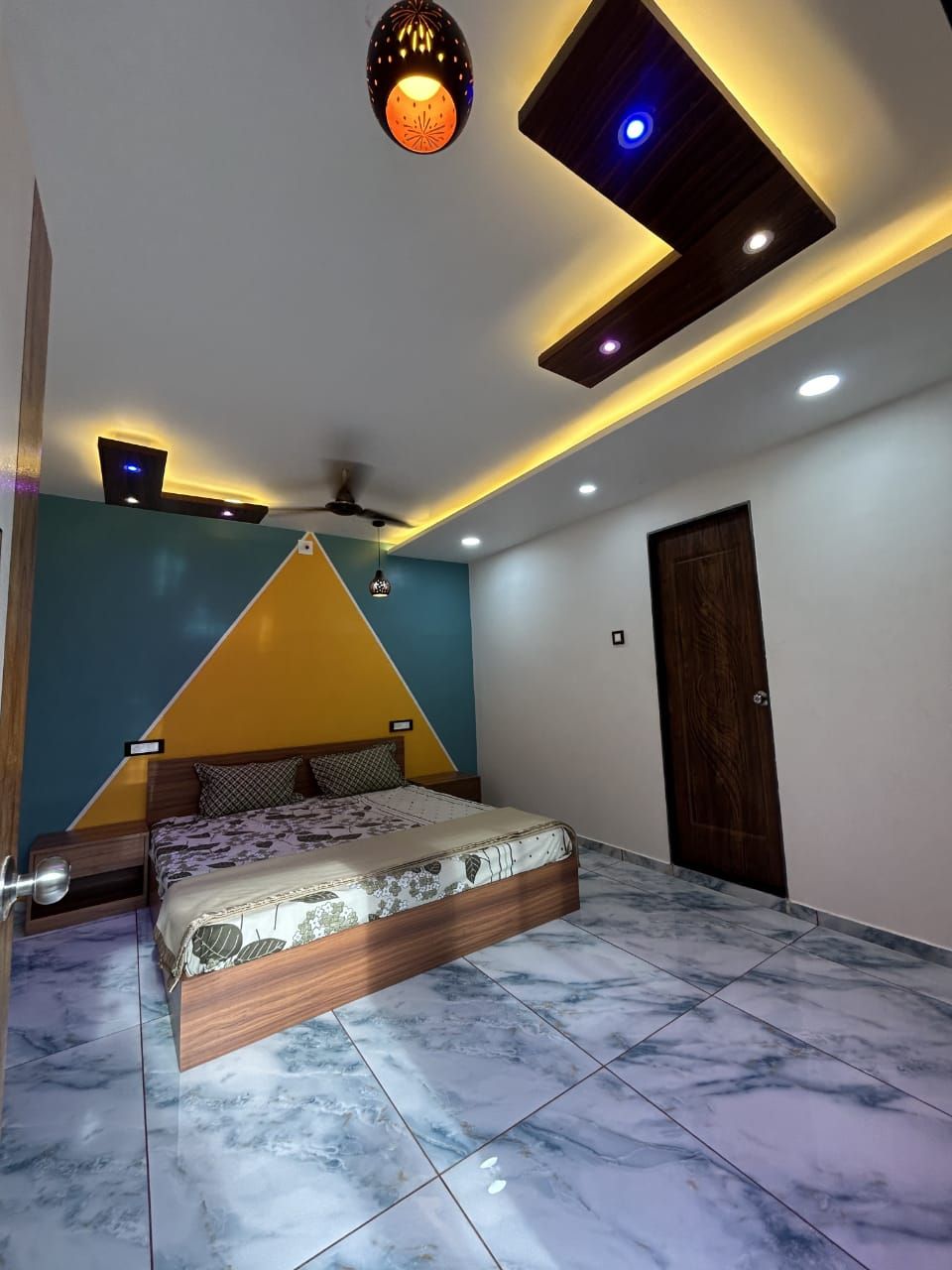 A bedroom with a bed, a ceiling fan, recessed lighting, a door, and a wall-mounted light fixture.