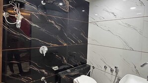 Een moderne badkamer met zwart marmeren wanden, een wit toilet, een wastafel en een douche.