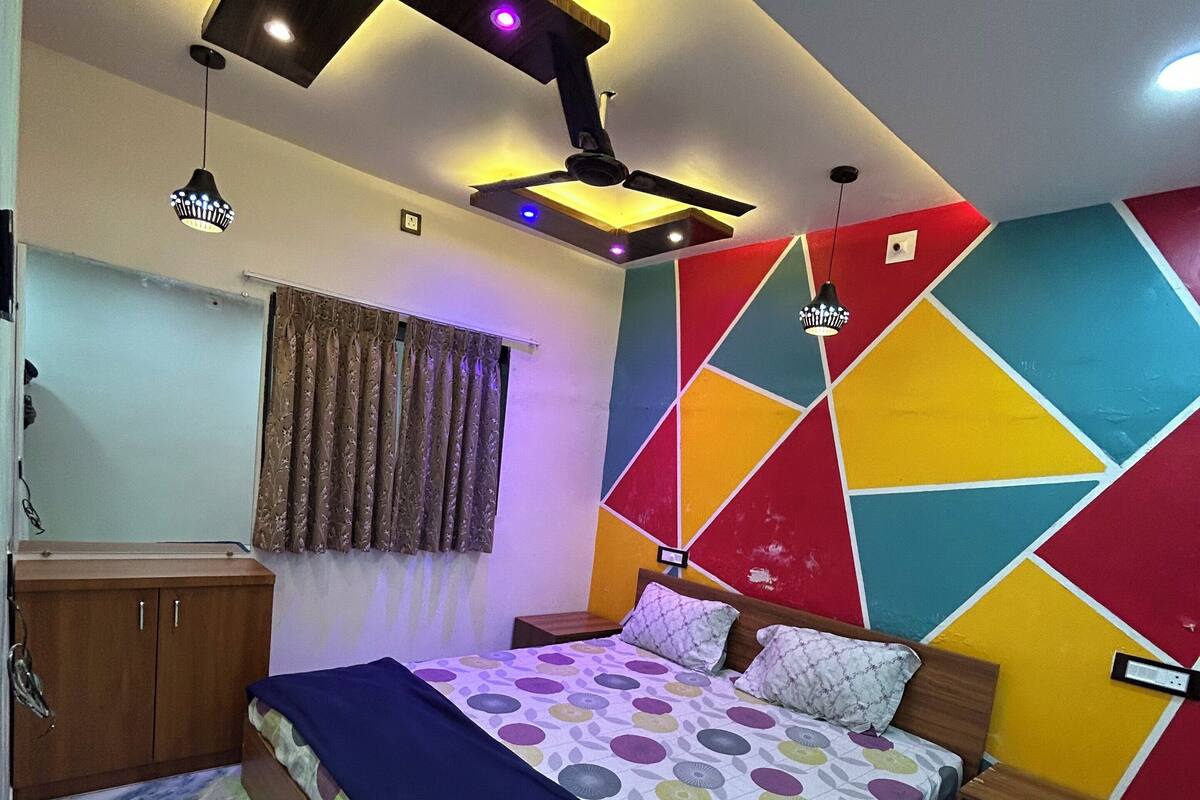 A bedroom with a bed, a wardrobe, a nightstand, a ceiling fan, and a wall with geometric patterns.