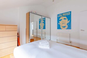 A hotel room with a bed, a wardrobe, a mirror, and a poster on the wall.