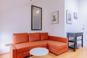 Un salon moderne avec un canapé d’angle, une petite table blanche et une table d’appoint en bois foncé.