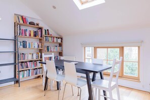 Une pièce comprenant une table à manger, des chaises blanches, une bibliothèque et une lucarne.