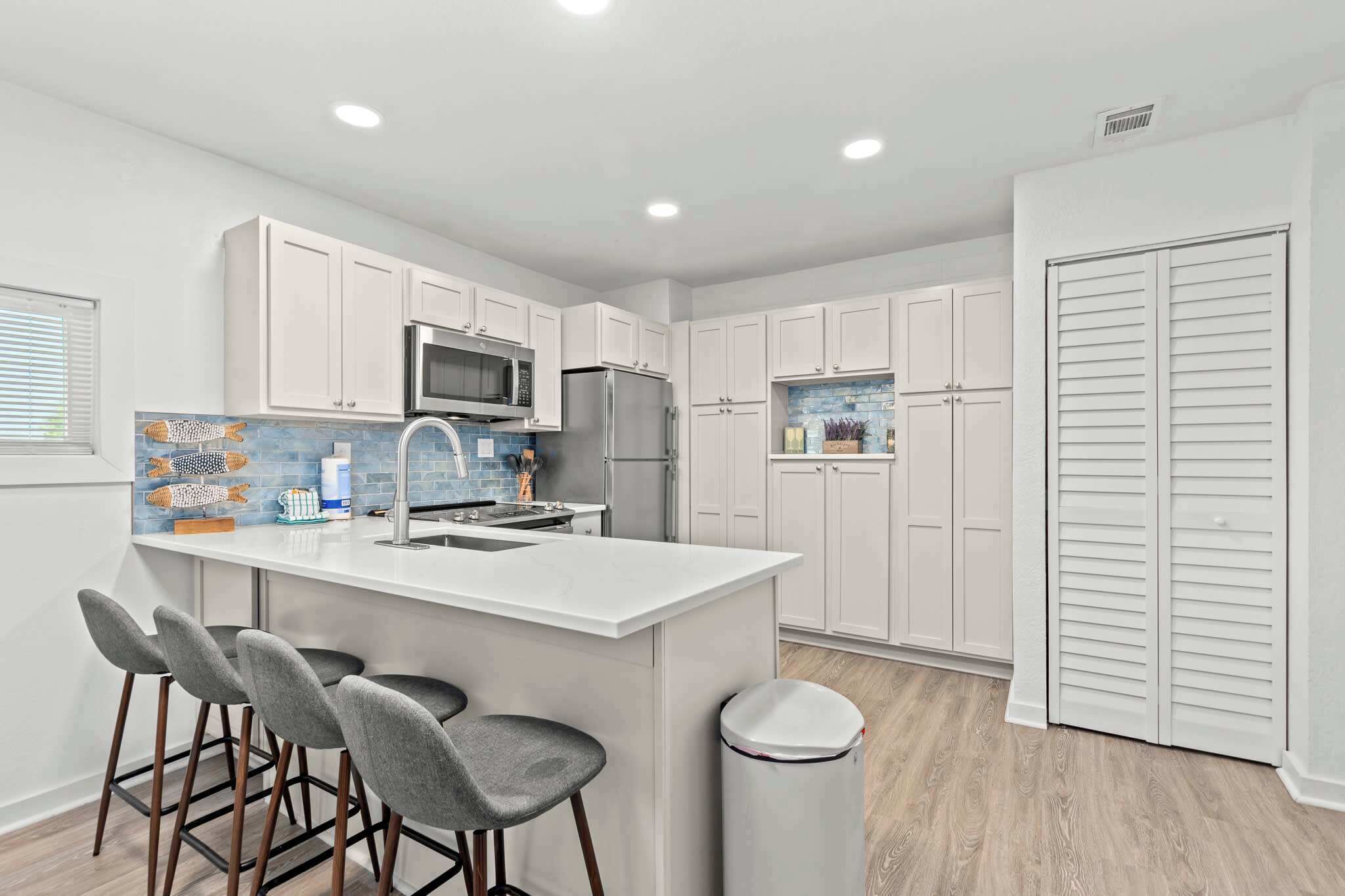 A modern kitchen with white cabinets, a central island with bar stools, a microwave, and a refrigerator.
