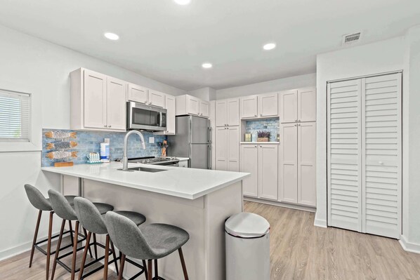 A modern kitchen with white cabinets, a central island with bar stools, a microwave, and a refrigerator.