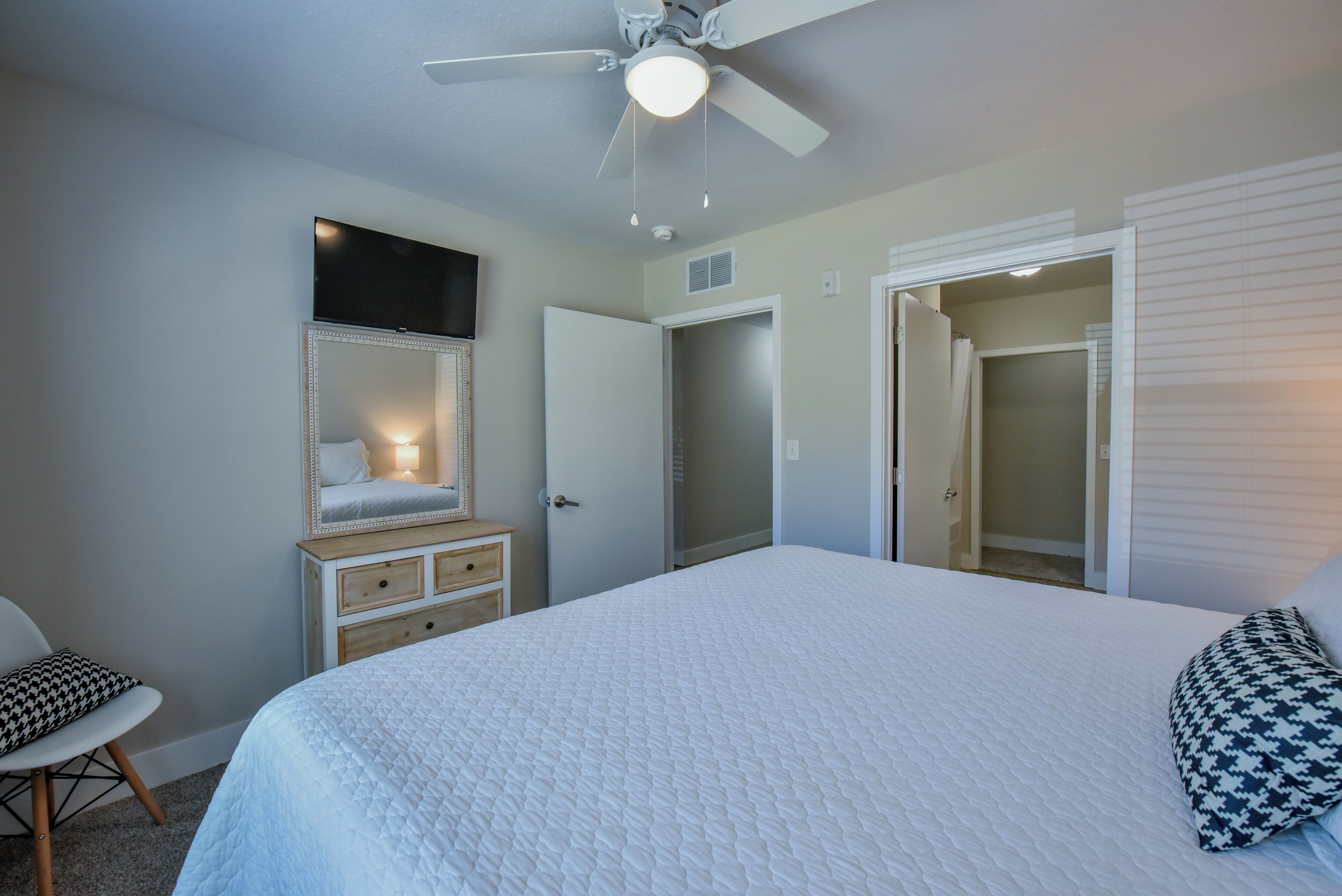 Un dormitorio con una cama grande, ventilador de techo, cómoda, espejo y vestidor.