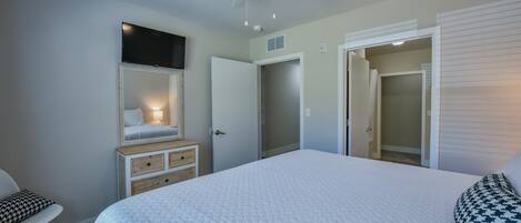 Un dormitorio con una cama grande, ventilador de techo, cómoda, espejo y vestidor.