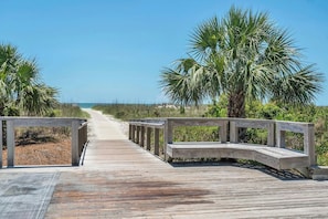 A wooden boardwalk leading to a beach with palm trees and a clear sky.
