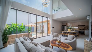 A modern living room with a sofa, coffee table, and a dining area with a table and chairs. - Zenithy 3BR Villa with Pool by NLA (Choeng Thale)