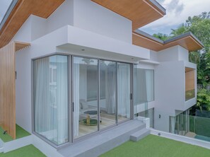 A modern house with large glass sliding doors, a balcony, and a small outdoor area with artificial grass.