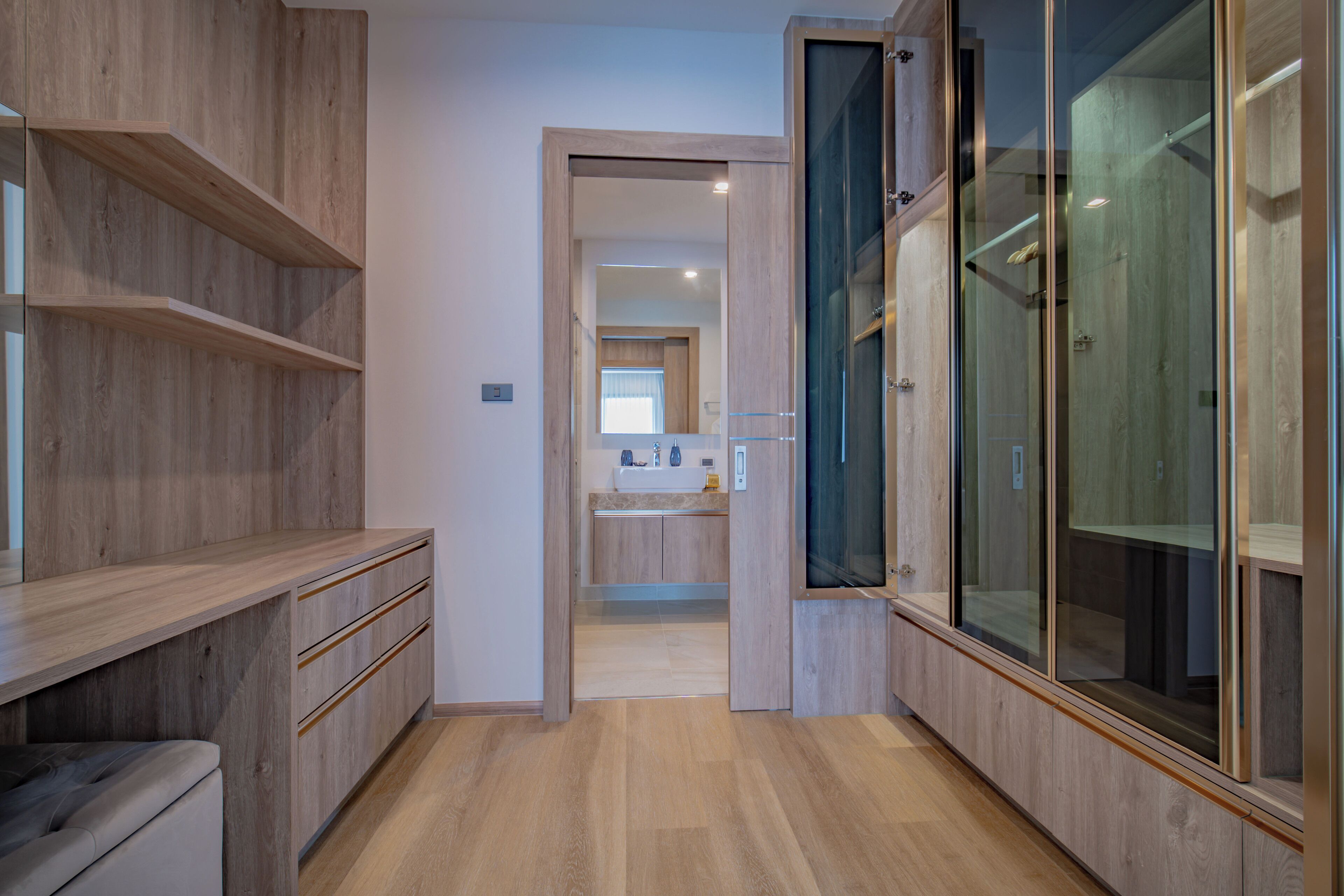 Un baño moderno con tocador de madera, cabina de ducha con mampara de vidrio y zona de lavamanos visible al fondo.