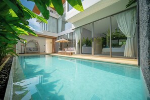 A modern pool area with clear water, a lounge chair, and a glass-enclosed room with a bed. - Zenithy 3BR Villa with Pool by NLA (Choeng Thale)