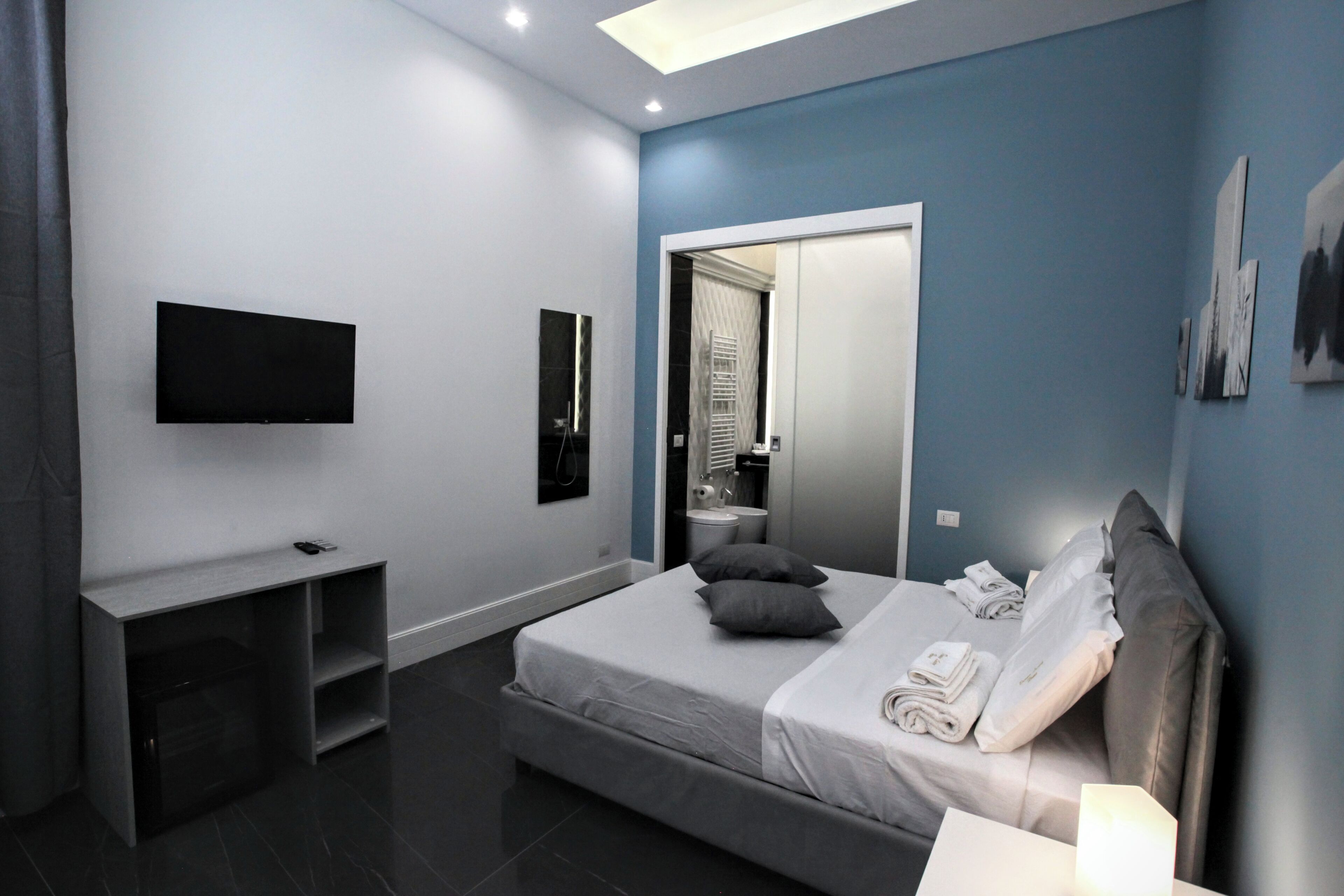 A modern bedroom with a bed, a TV mounted on the wall, a desk, and a mirror.