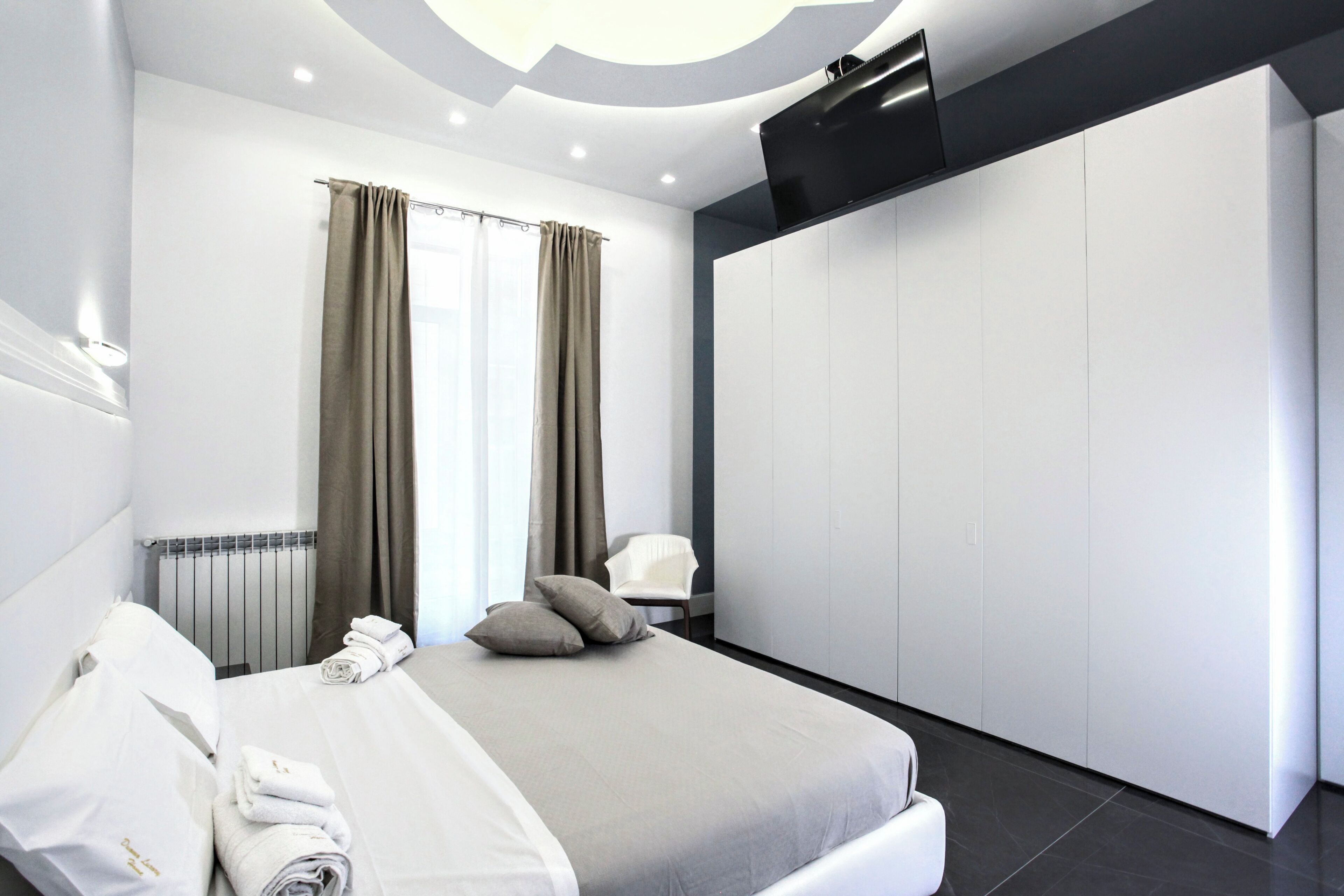 A modern hotel room with a neatly made bed, a chair, and a large wardrobe.