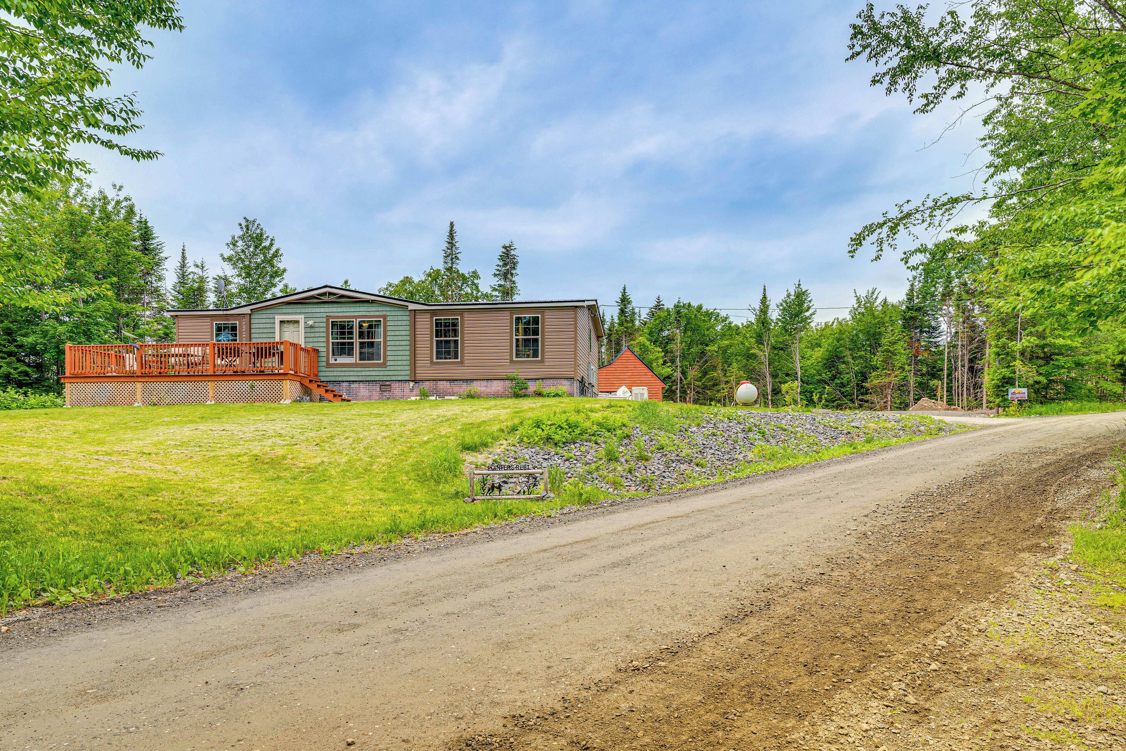A two-story house with a wooden deck and a dirt road in front.