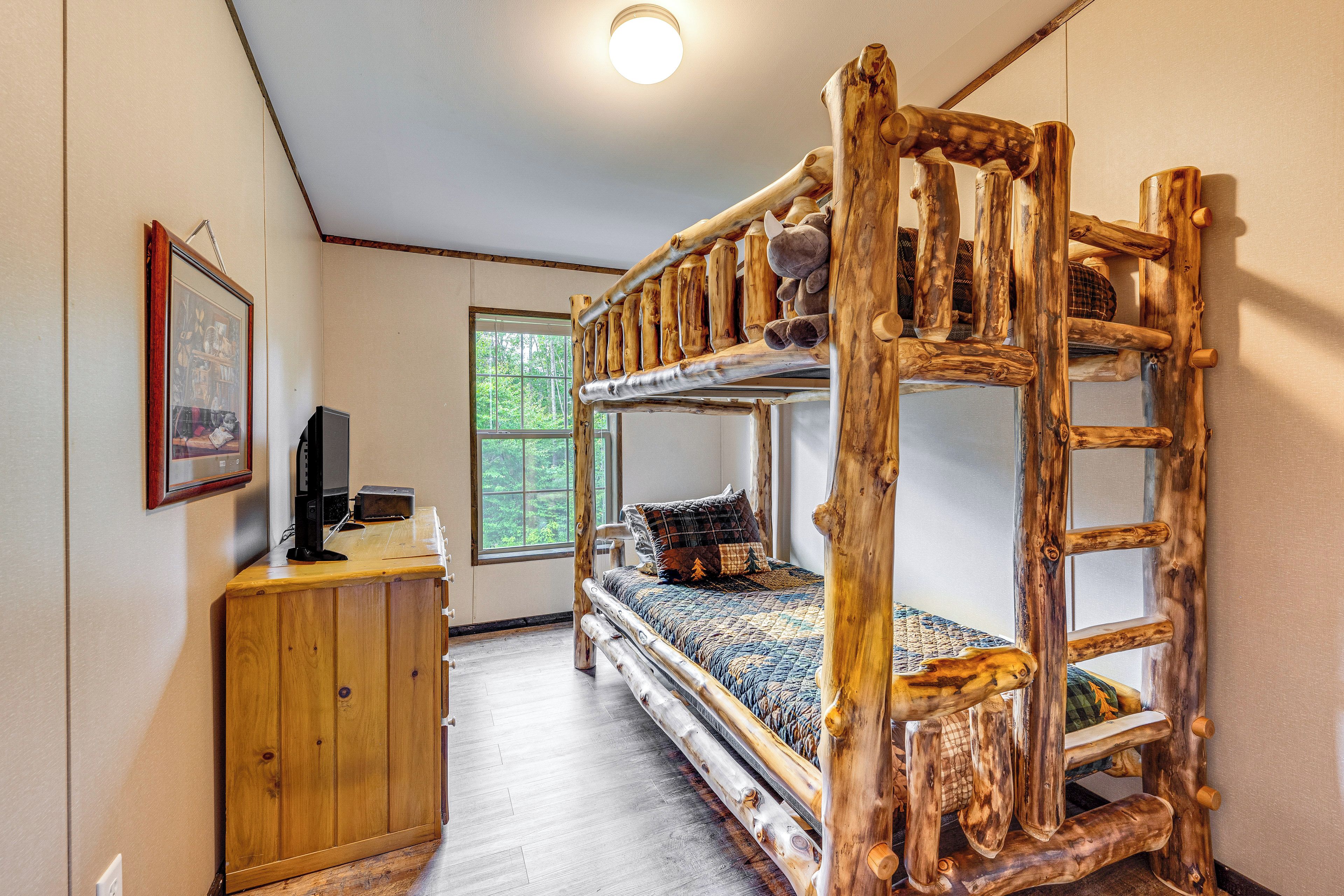 A rustic wooden bunk bed with a ladder, a wooden desk with a computer, and a framed picture on the wall.