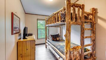 A rustic wooden bunk bed with a ladder, a wooden desk with a computer, and a framed picture on the wall.