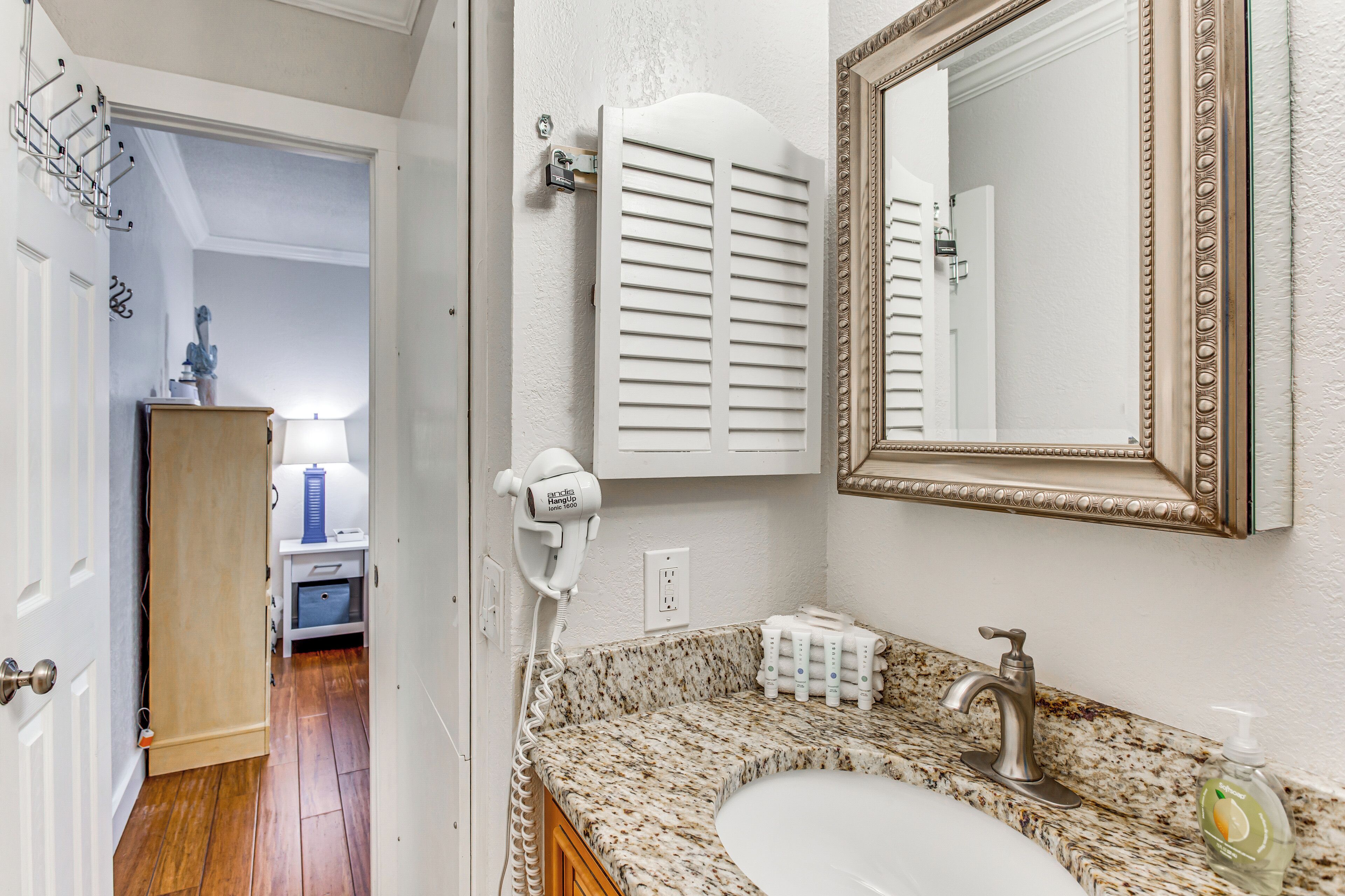A bathroom with a granite countertop sink, a mirror with an ornate frame, and a hairdryer on the wall.