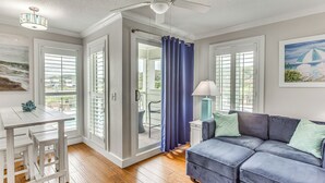 A modern living room with a grey sofa, a white table with stools, and a ceiling fan. - On-site Ocean Access: Condo in Myrtle Beach (Myrtle Beach)