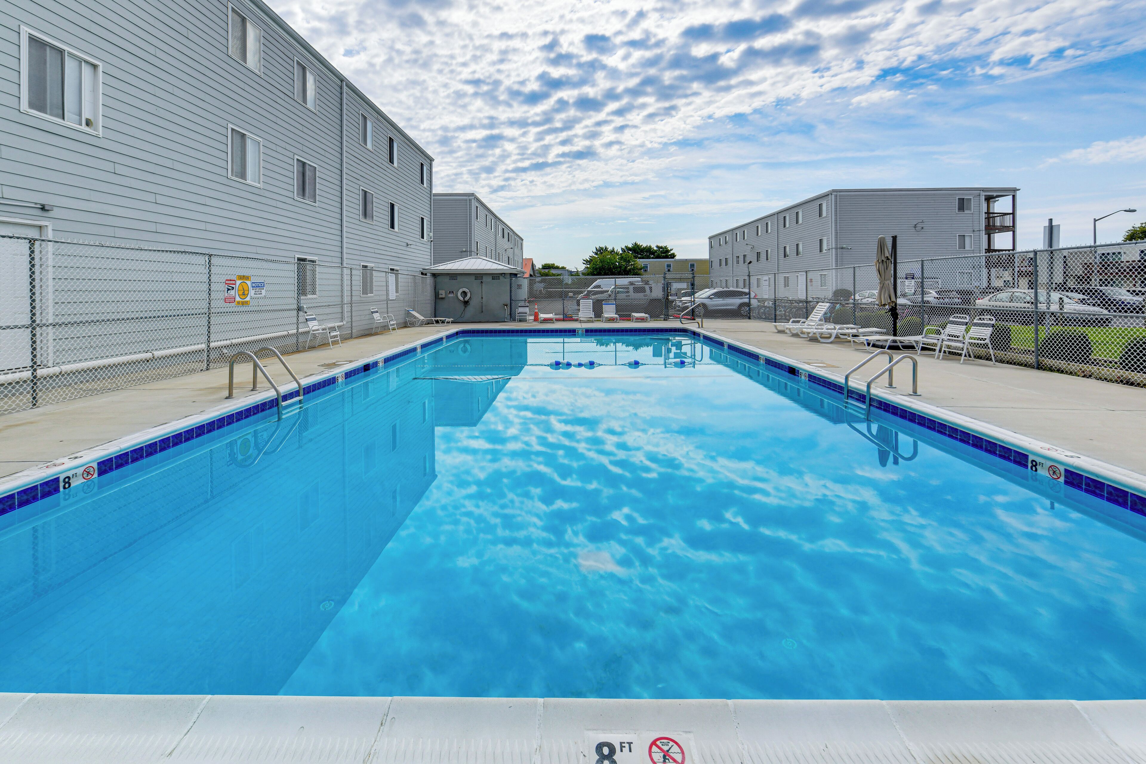 Ein rechteckiger Pool mit blauer Fliesenbordur, umgeben von einem Drahtzaun, neben einem Gebäude mit flachem Dach.