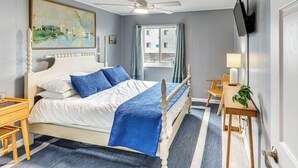 A bedroom with a bed, a desk, a chair, a television, and a window with curtains.