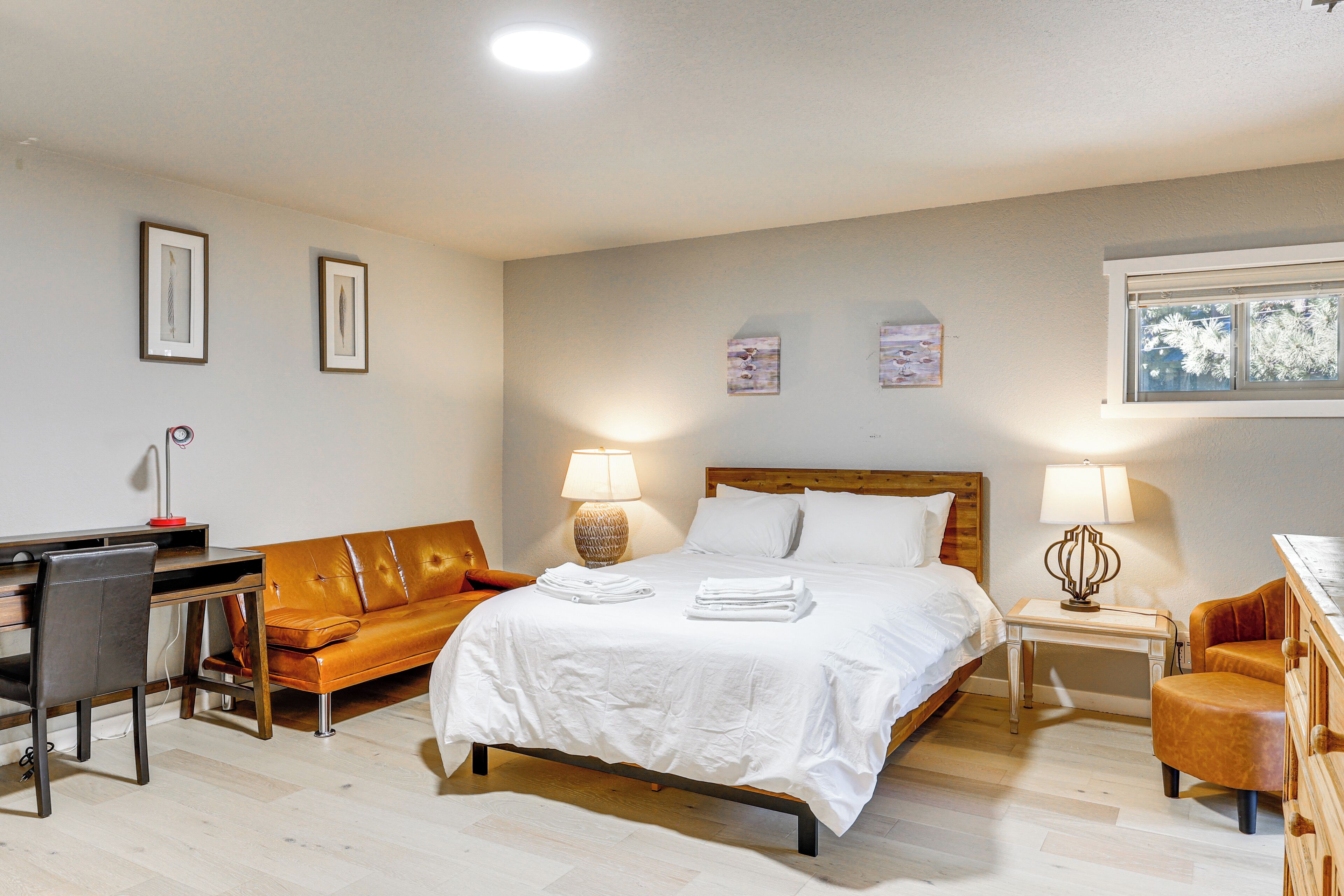 A bedroom with a bed, a desk, a chair, a sofa, and two bedside tables with lamps.