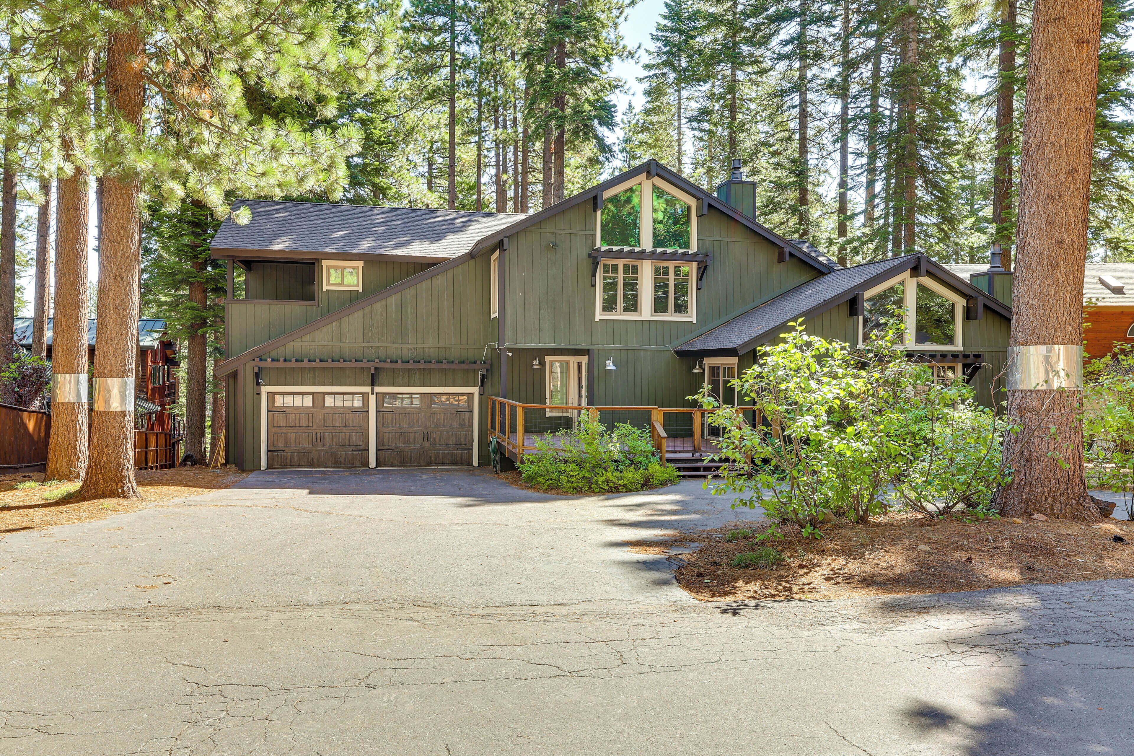 A two-story house with a garage, surrounded by tall trees.