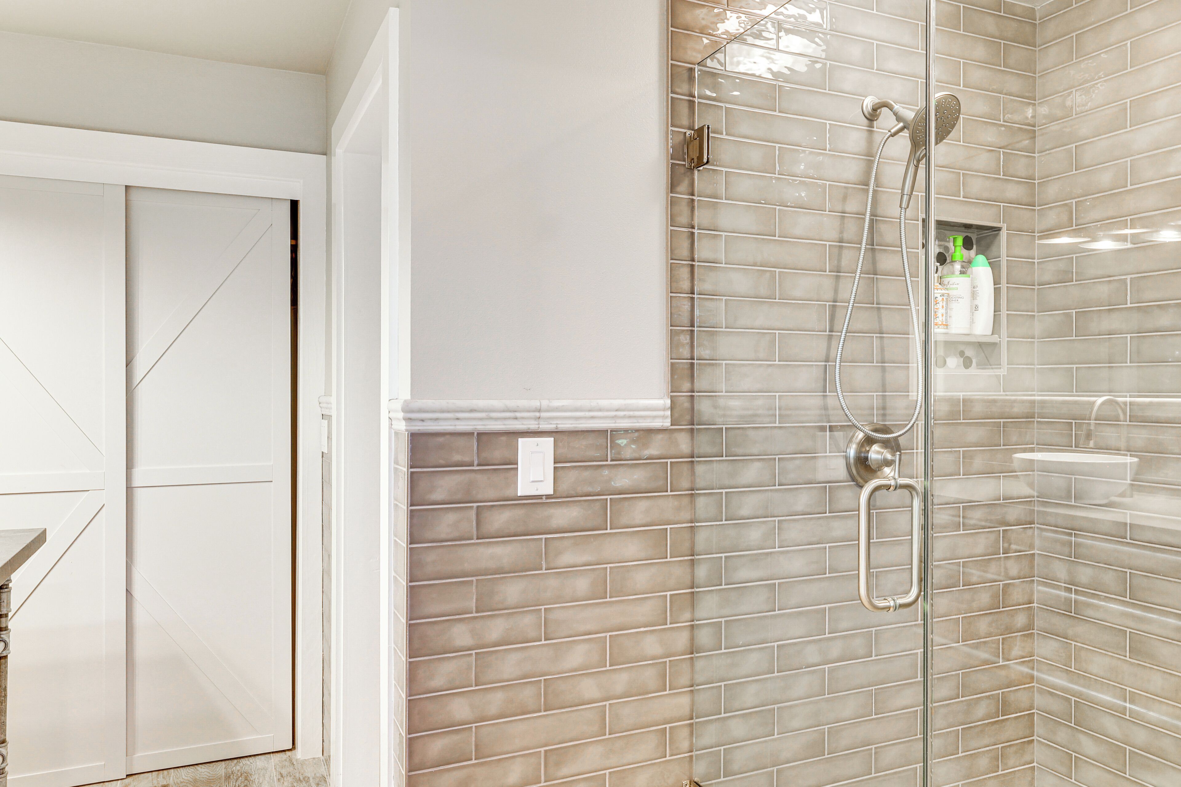 A bathroom with a glass shower enclosure, a white sink, and a tiled wall.