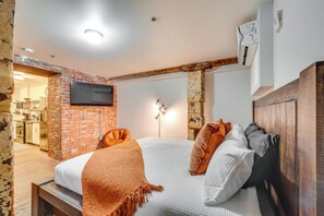 A bedroom with a brick wall, a flat-screen TV mounted above the bed, a wooden headboard, and a bedside table. - Dtwn Knoxville Studio Half-mi to Market Square! (Knoxville)