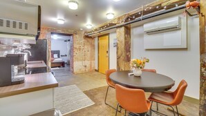 A modern kitchen with a coffee machine, a dining area with a round table and orange chairs, and a brick wall with exposed pipes. - Dtwn Knoxville Studio Half-mi to Market Square! (Knoxville)