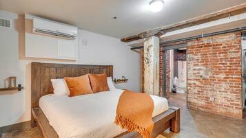 A bedroom with a wooden bed, a white wall-mounted air conditioner, and a brick wall.