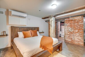 A bedroom with a wooden bed, a white wall-mounted air conditioner, and a brick wall. - Dtwn Knoxville Studio Half-mi to Market Square! (Knoxville)