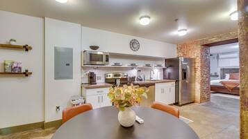 A modern kitchen with white cabinets, a microwave, a refrigerator, and a dining area with a table and chairs.